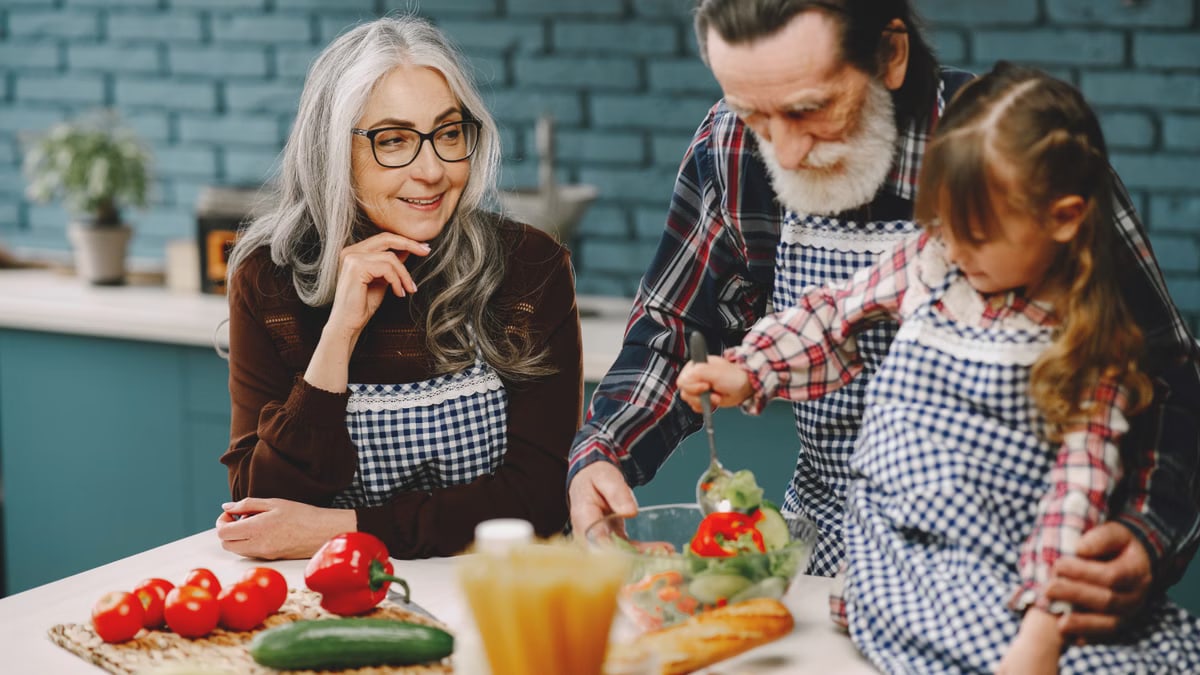 Grandparents and a child enjoy cooking together in a warm kitchen setting.